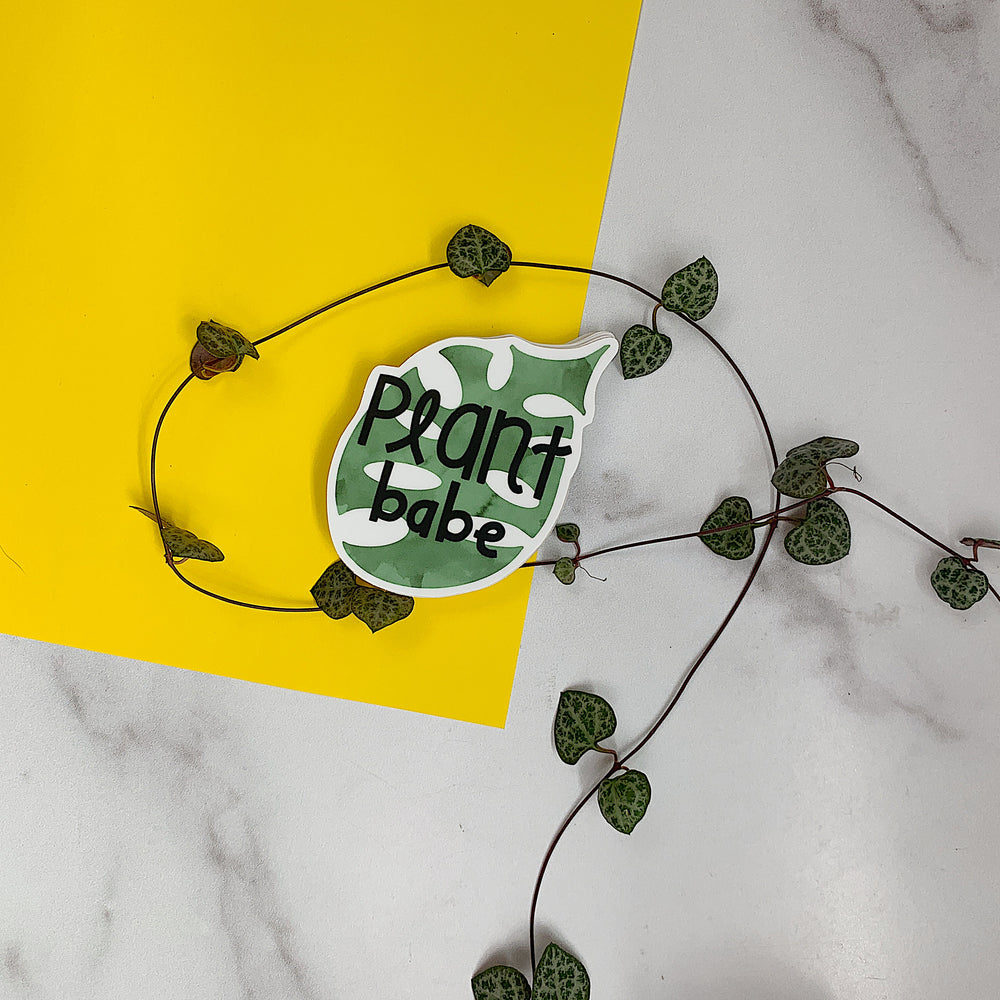 Decorative sign with 'Plant babe' text on a yellow and white marble background