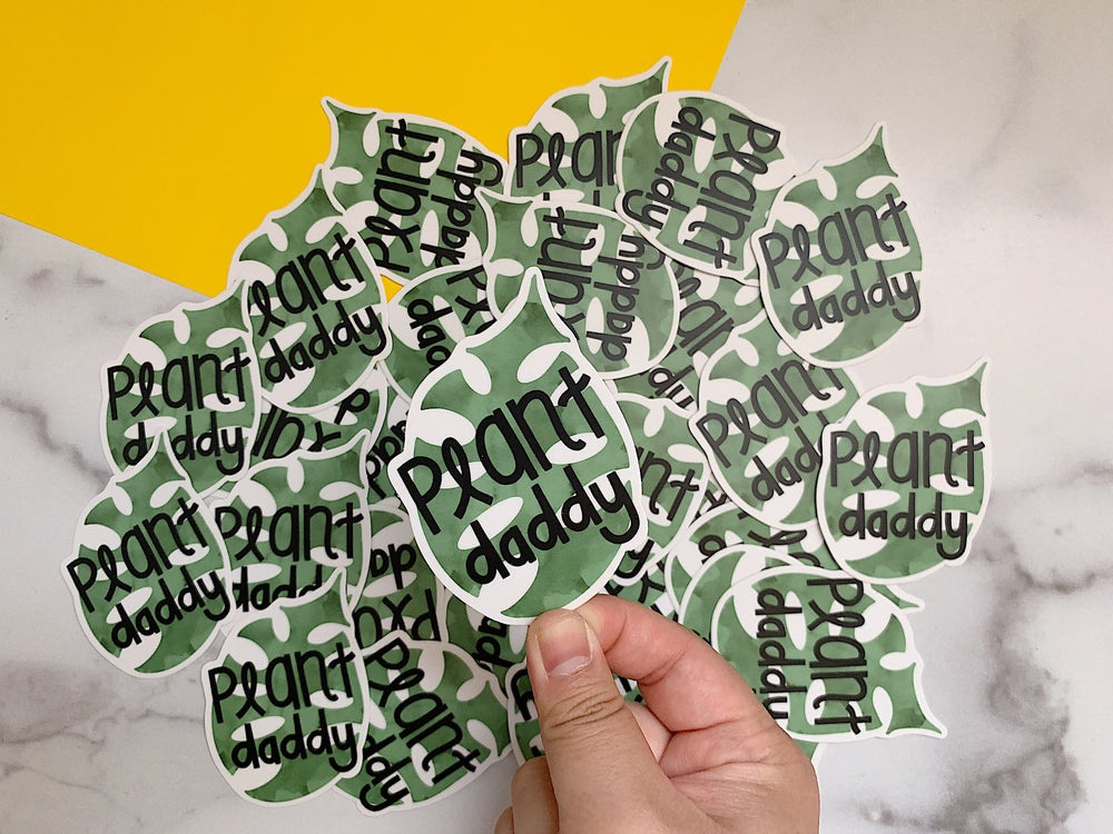 Multiple 'Plant daddy' stickers with a hand holding them against a marble background.