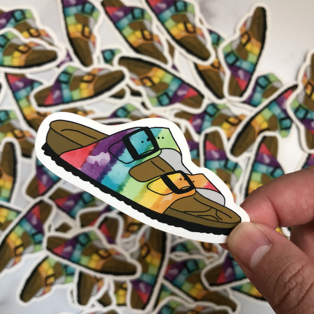 Rainbow Sandal Sticker being held by someone with a pile of the same stickers in the background